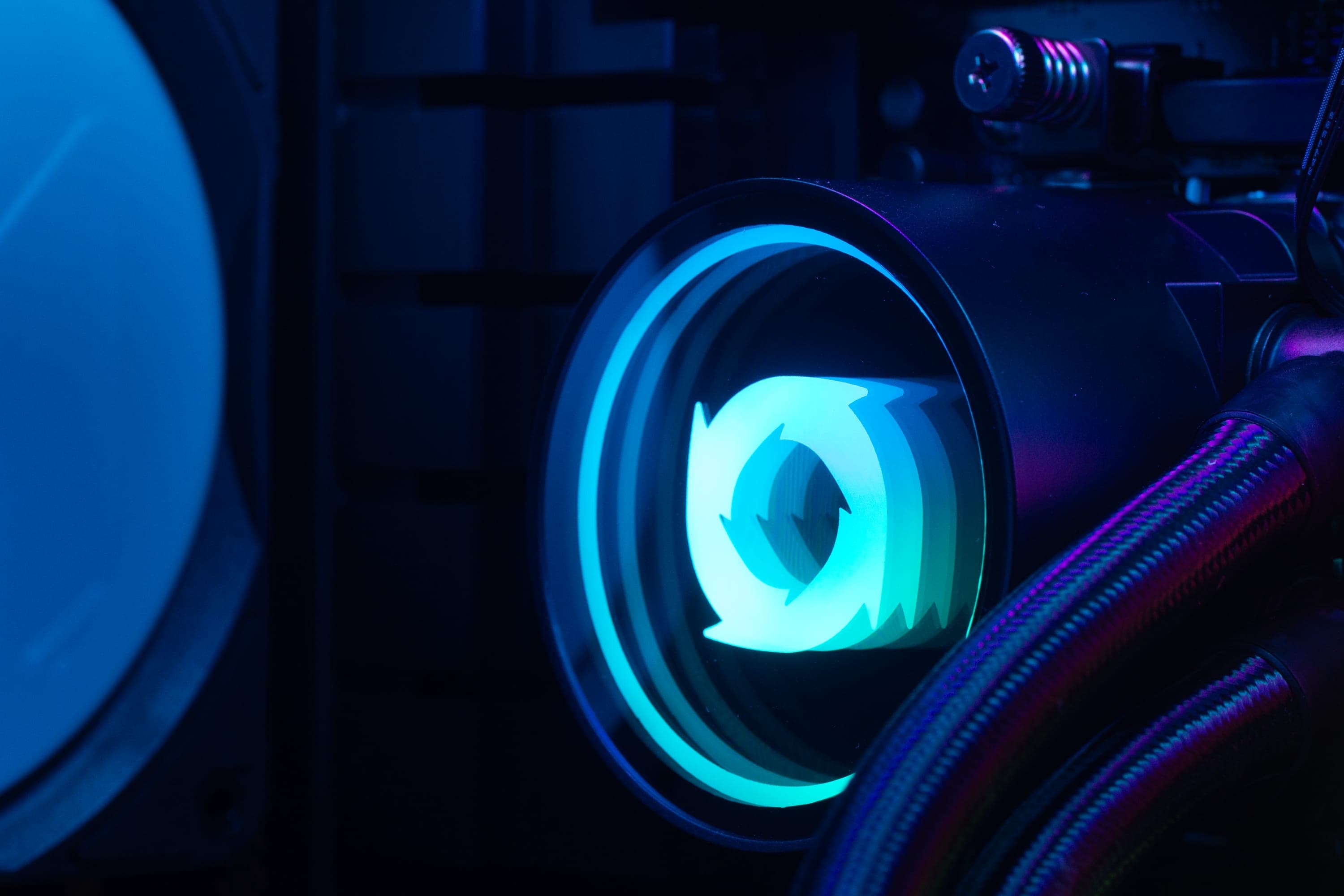 The pump block of a Typhoon PYOF 360 cooler fitted in a build, the Typhoon mark lit in its cap, with braided coolant lines and a radiator fan behind.